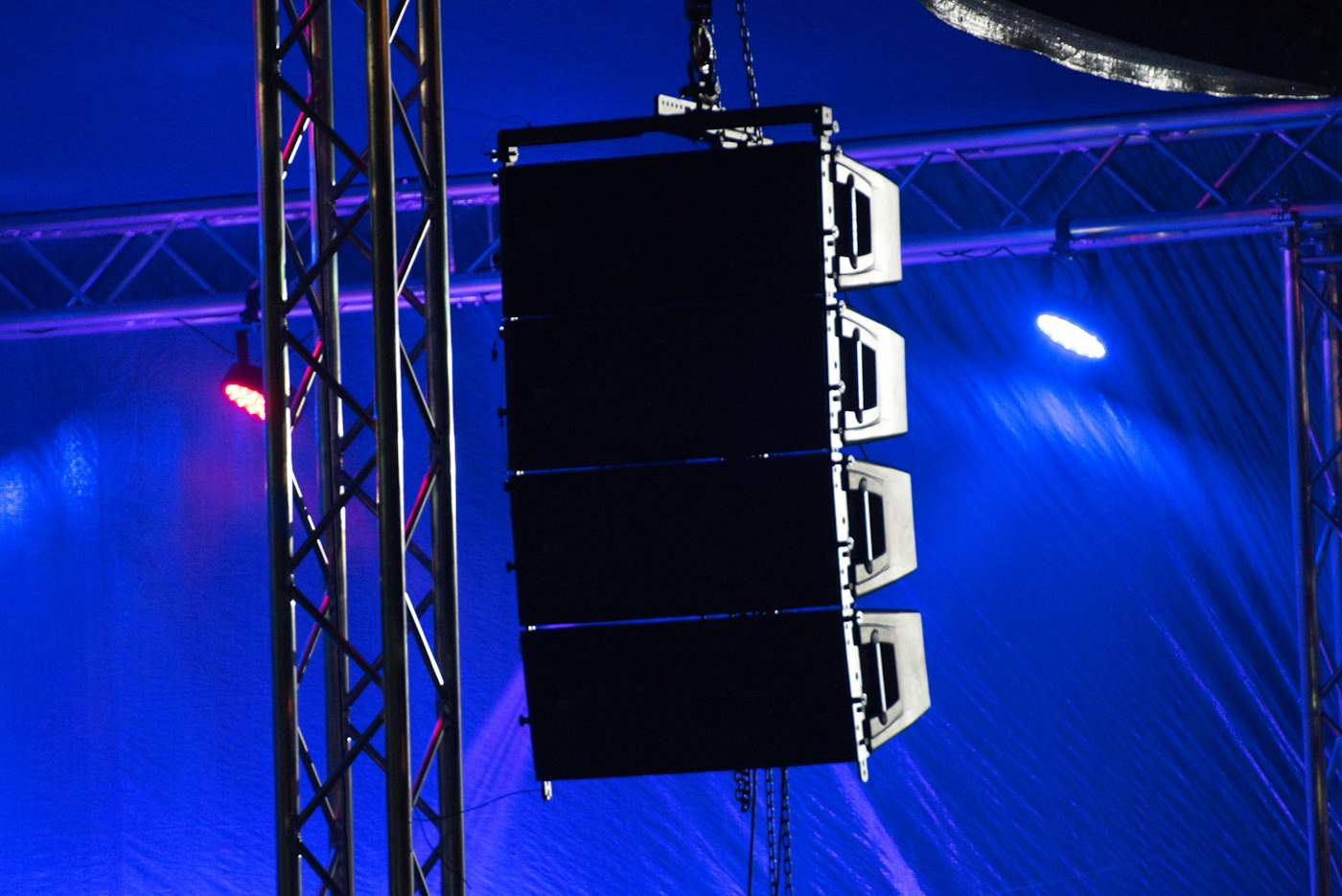 Flown line-array speaker cluster hanging from truss under blue stage lighting