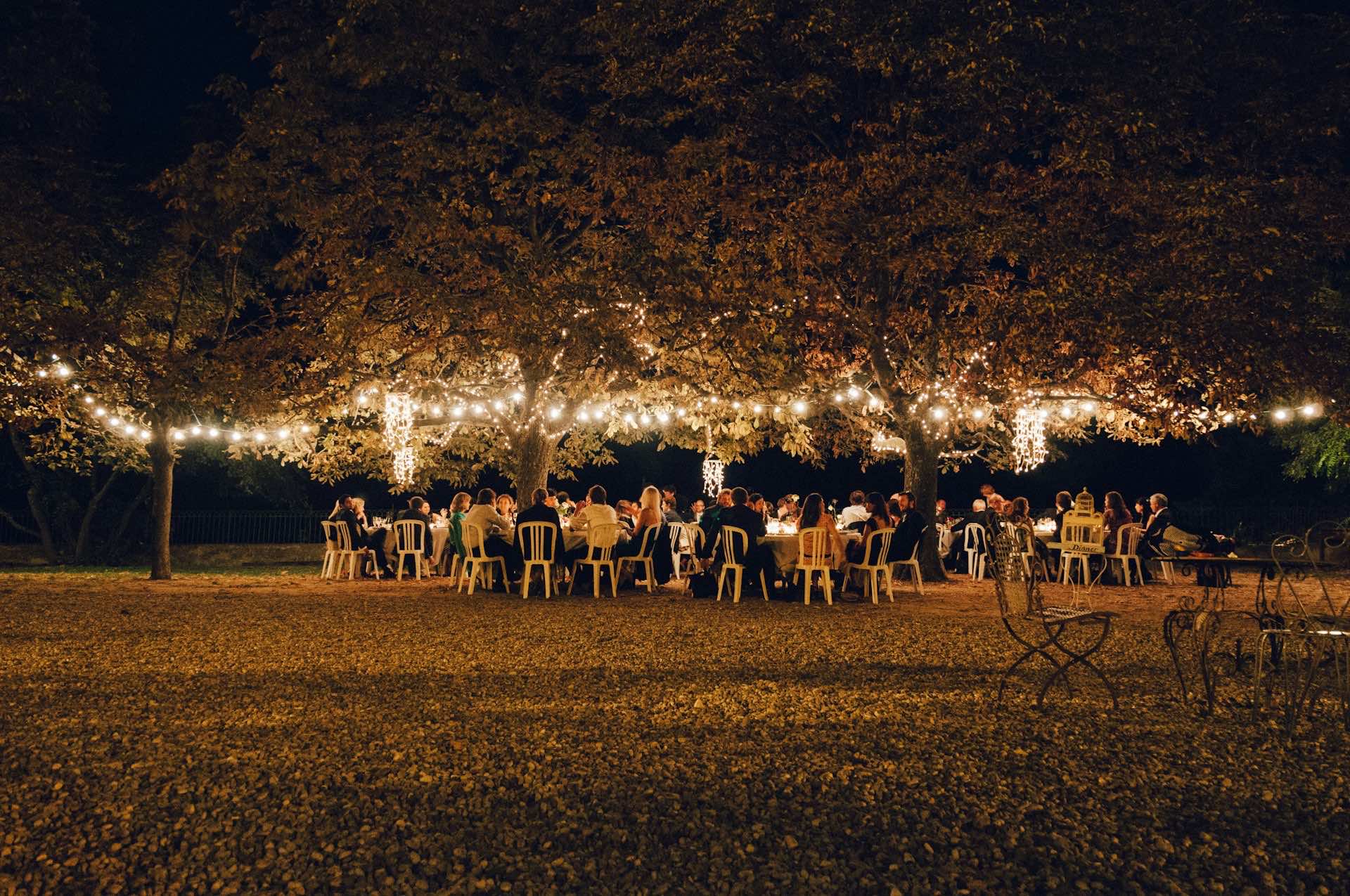 Outdoor evening dinner under warm string lights strung between trees