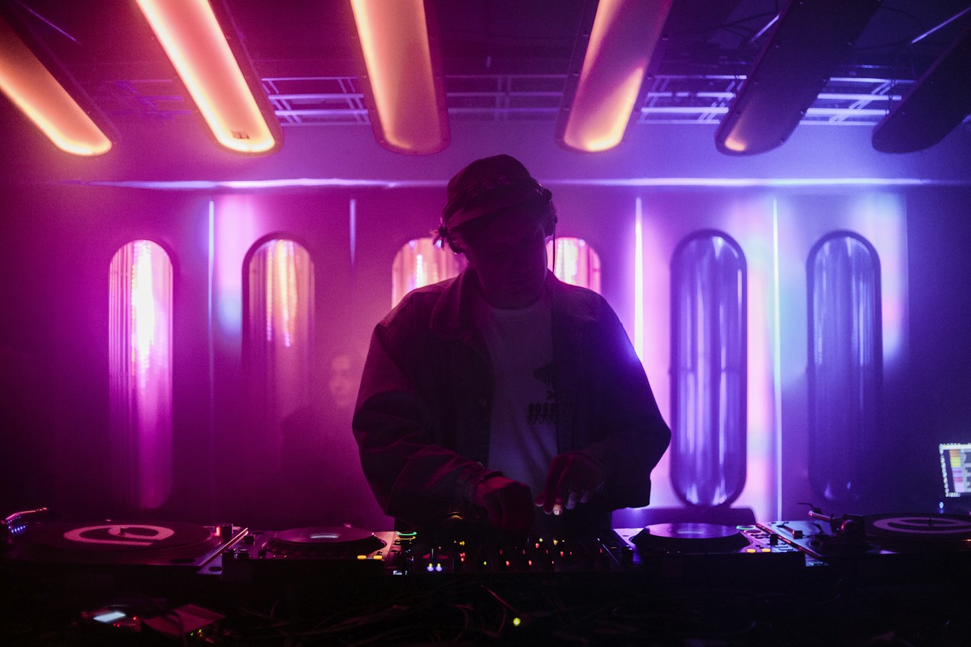 DJ at the decks silhouetted against pink and purple stage lighting