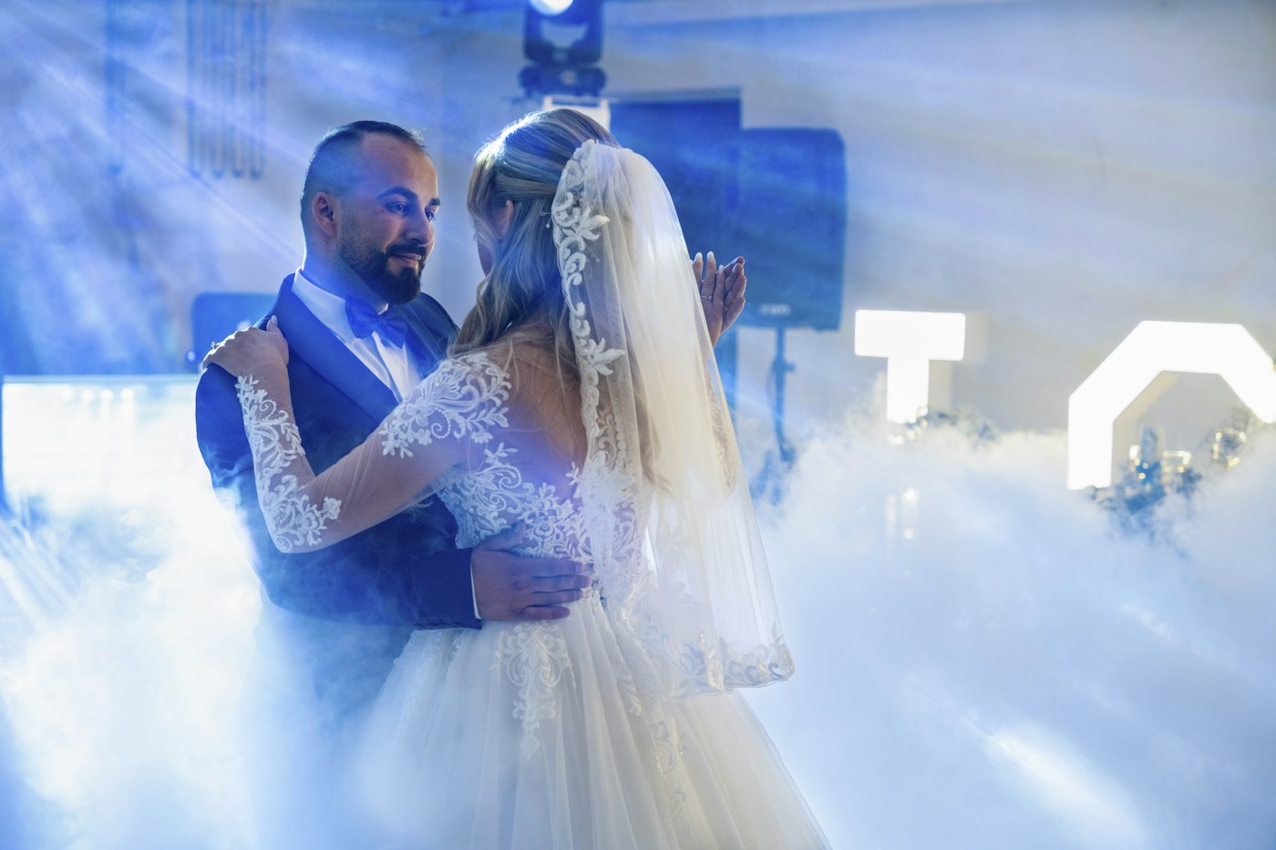 Bride and groom dancing in a cloud of low-lying fog lit by blue light