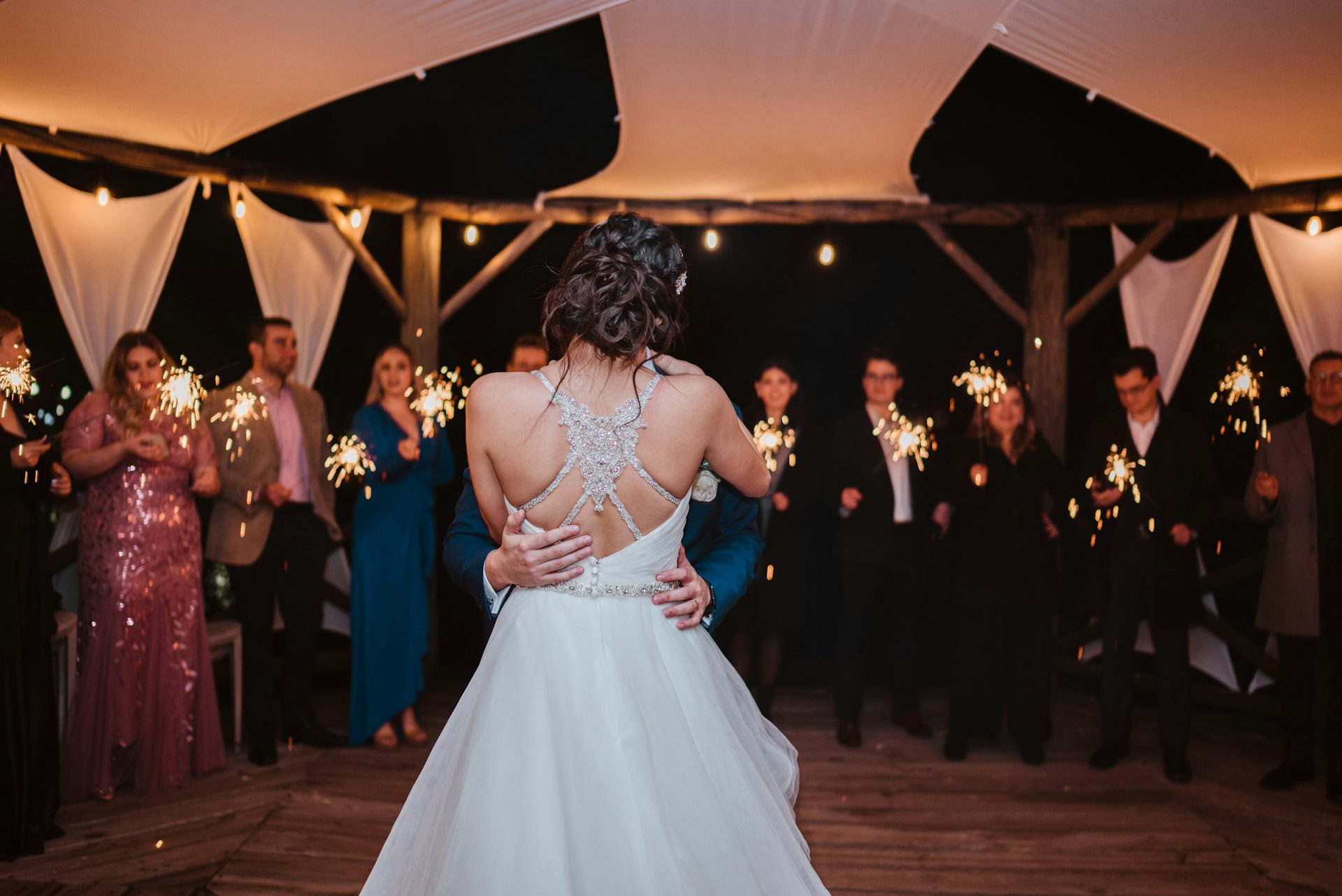 Bride and groom share a first dance at night while guests around them hold lit sparklers