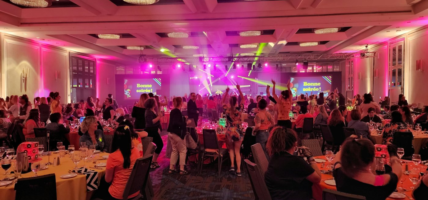 Ballroom dance floor with guests dancing under pink uplighting and moving-head beams, with LED screens beside the stage